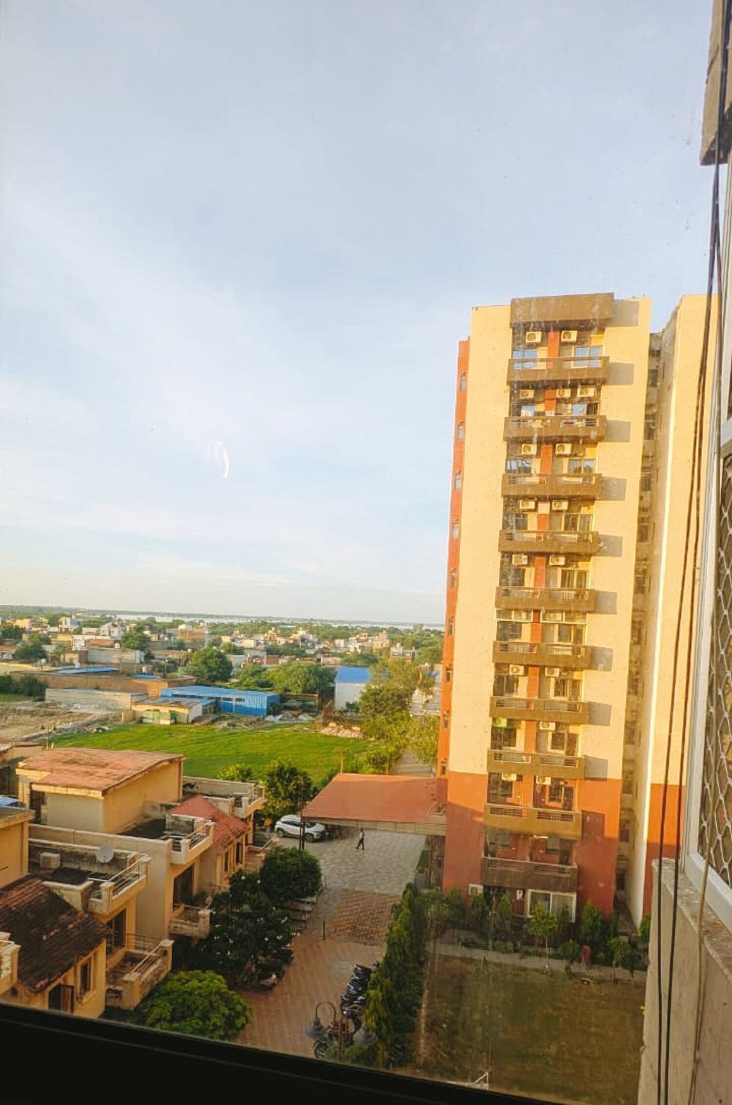A high-rise building with multiple balconies, a courtyard with greenery, and a view of a distant town.