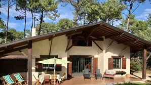 Ein rustikales Haus mit überdachter Terrasse, Sitzgelegenheit im Freien und Schornstein.