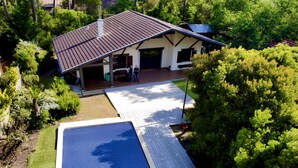 Ein Haus mit überdachter Terrasse, Schwimmbad und Garten.