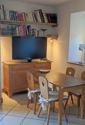 A dining area with a wooden table and chairs, a television on a wooden cabinet, and bookshelves above. - Odette's barn (BOURG-SAINT-MAURICE)
