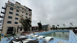 A hotel with a swimming pool, lounge chairs, and a building with multiple windows and balconies.