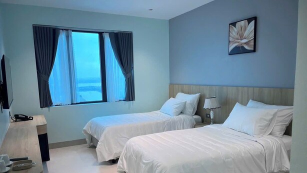 A hotel room with two beds, a desk, a lamp, and a window with curtains.