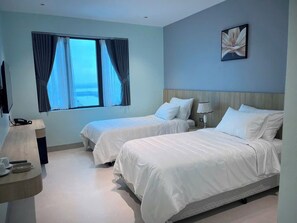 Ein Hotelzimmer mit zwei Betten, einem Schreibtisch, einer Lampe und einem Fenster mit Vorhängen.