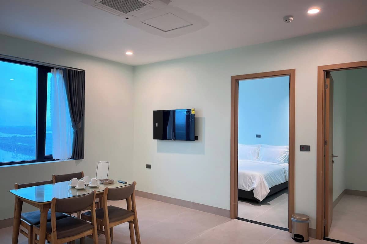 Ein Hotelzimmer mit Bett, Wandfernseher, Esstisch mit Stühlen und einem fensterbepflanzten Fenster.