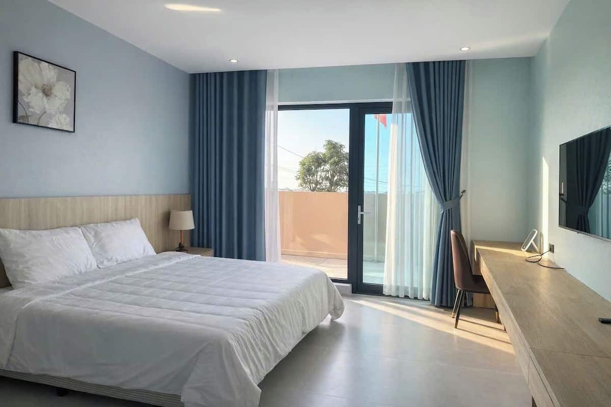 Ein Hotelzimmer mit Bett, Schreibtisch, Stuhl, Fernseher und einem Balkon mit Vorhängen.