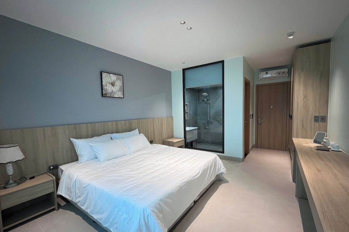 Ein modernes Hotelzimmer mit Bett, Nachttisch, Ablagefläche und einer integrierten Duschkabine.
