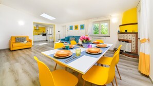 Un comedor luminoso con sillas amarillas, una mesa blanca y una cocina al fondo.