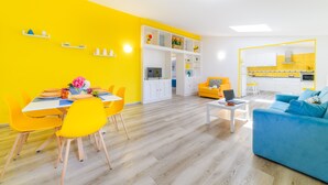 Un interior luminoso en amarillo y blanco con una zona de comedor, un sofá y una cocina.