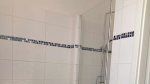 Un baño con inodoro, ducha con puerta de vidrio y paredes de cerámica.