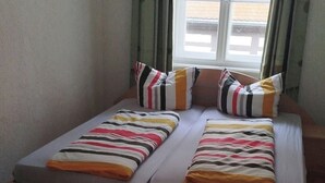 Una cama con ropa de cama a rayas y almohadas, una ventana con cortinas y vistas a edificios.