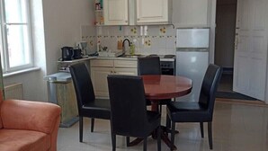 Cocina compacta con armarios blancos, una mesa de comedor con sillas y un sofá en una habitación luminosa con piso de baldosas.