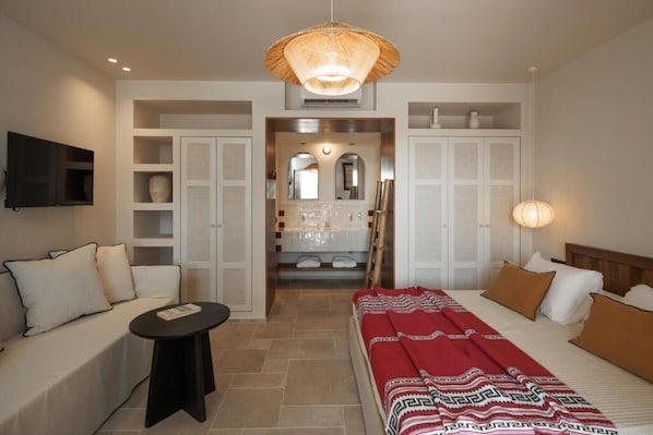 A hotel room with a bed, a sofa, a small table, a TV, and a bathroom visible through an open door.
