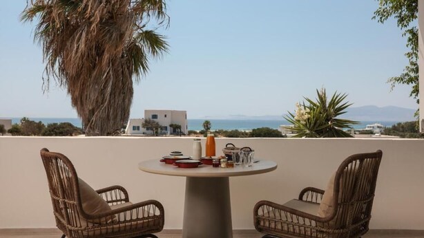 Ein Balkon mit Korbstühlen, einem runden Tisch und Blick auf das Meer und die Gebäude.