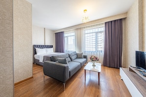 Una habitación de hotel moderna con cama, sofá gris, mesa de centro y televisor.