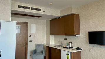 Een compacte woonruimte met een kitchenette, een bank, een klein tafeltje met een fles en een aan de muur bevestigde televisie.