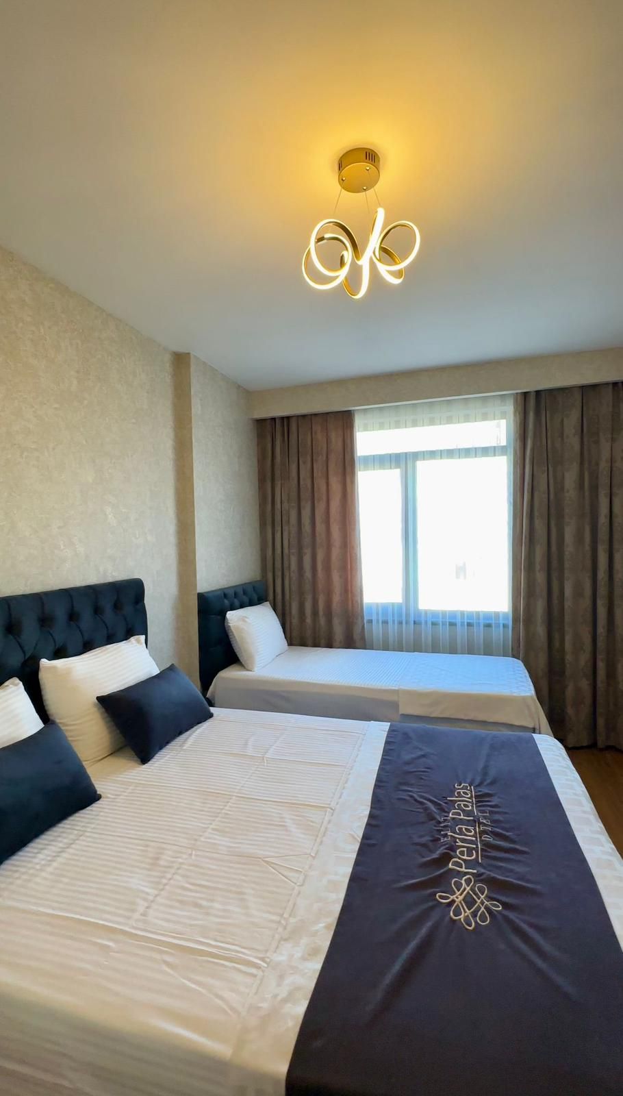 Een hotelkamer met twee bedden, een groot raam met gordijnen en een plafondlamp.