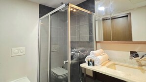 A modern bathroom with a glass-enclosed shower, a toilet, a sink with toiletries, and a mirror.