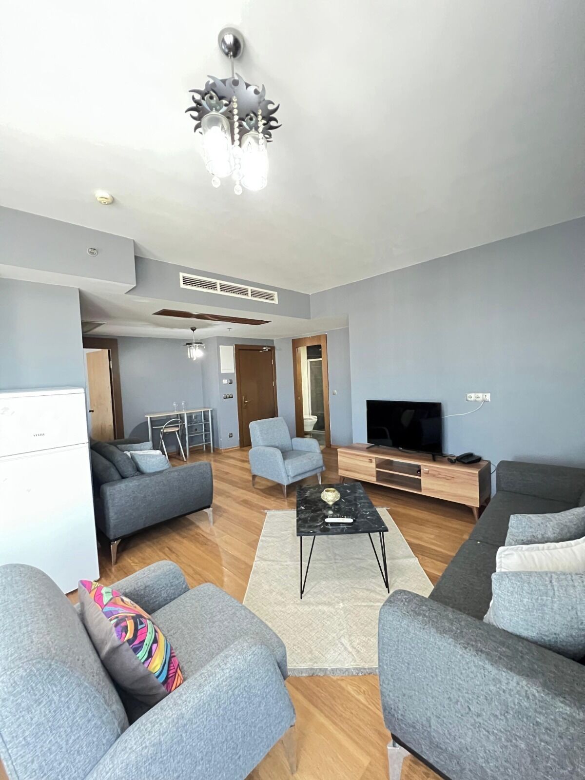Un salon moderne avec des canapés gris, une table basse, un téléviseur et un ventilateur de plafond.