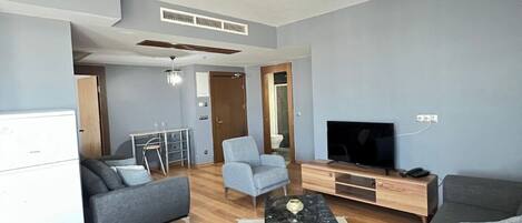 Una sala de estar moderna con sofás grises, una mesa de centro, un televisor y un ventilador de techo.
