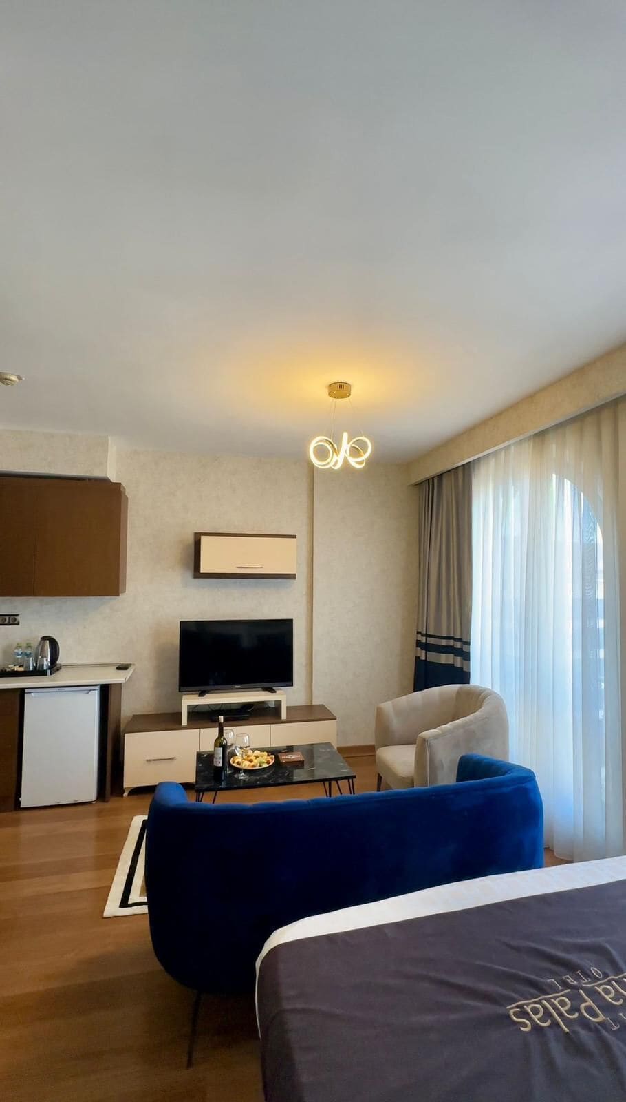 Habitación de hotel con cama, televisor, escritorio con tetera, silla y sofá.