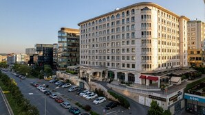 A multi-story hotel with a classic architectural style, featuring a central courtyard and a parking lot with several cars.