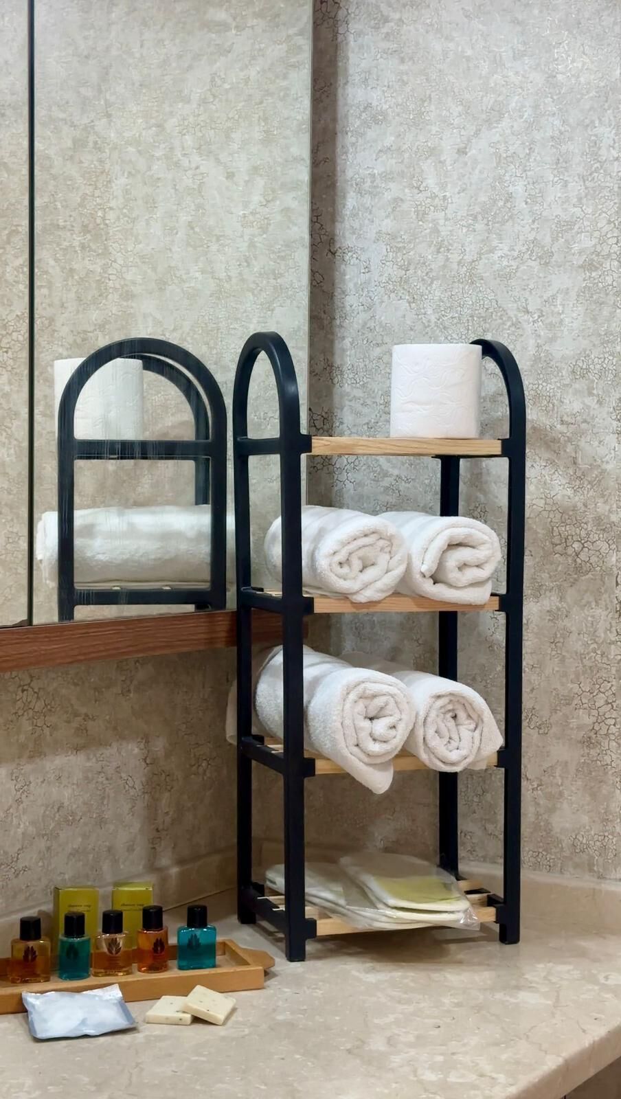 A bathroom with a towel rack holding rolled towels, a toilet paper roll, and a mirror.