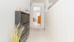 Een smalle gang met een donkere kast, een plant en een deur naar een andere kamer.