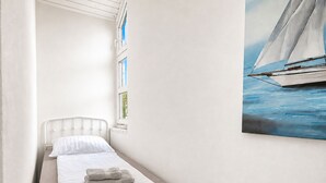 A small, single-bed room with a window, a painting of a sailboat, and a neatly made bed. - fewo1846 - Pirate's Cabin / Centrally Located Apartment in an Older Building for Up to 4 People (Flensburg)