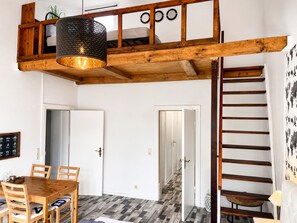 A room with a wooden ceiling, a dining table with chairs, a hanging light fixture, and a staircase. - fewo1846 - Pirate Cabin / Central apartment in a historic building for 4 people (Flensburg)