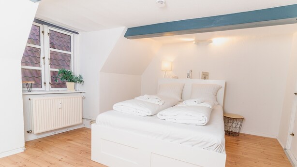 Un dormitorio con cama, radiador, ventana con planta y mesita de noche.