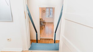 Una escalera conduce a una habitación con piso de madera, un reloj en la pared y una ventana.