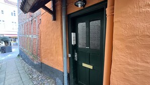 A building with a brick facade, a black door with a brass handle, and a small window with a light fixture above it. - fewo1846 - Matrosenkoje - Centrally Located Apartment in an Older Building for 2 People on the 2nd Floor (Flensburg)