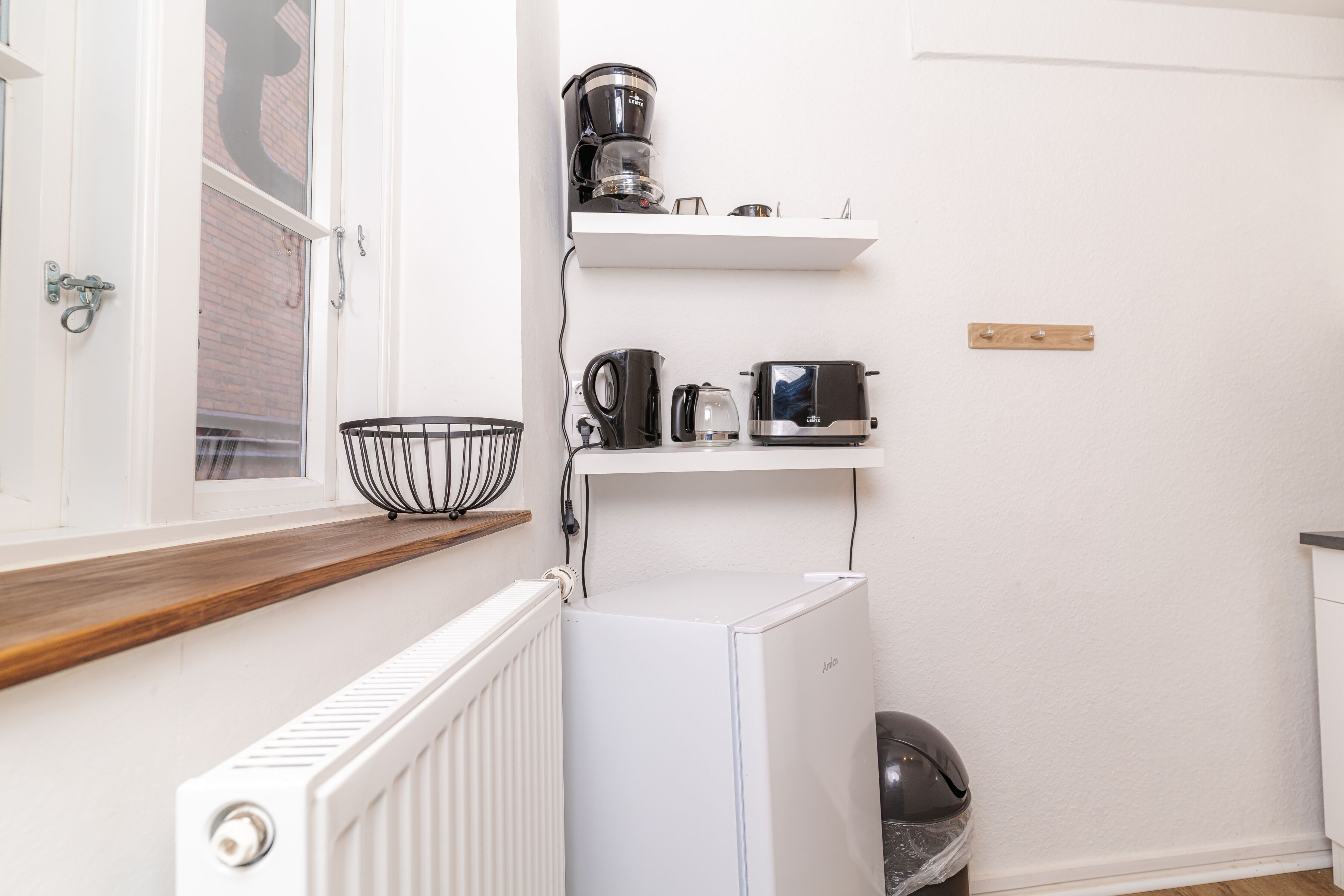 Een kleine keuken met een witte koelkast, een koffiezetapparaat, een broodrooster en een waterkoker op een witte plank.
