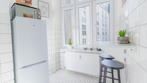 Una cocina moderna con un refrigerador blanco, una ventana que da a vista de edificios y dos taburetes de bar.