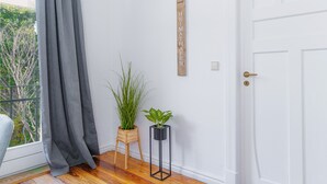 Una habitación con piso de madera, una puerta blanca, una cortina gris, una planta en maceta y un letrero de madera con texto.