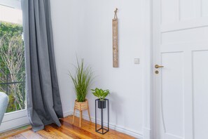A room with a wooden floor, a white door, a grey curtain, a potted plant, and a wooden sign with text. - fewo1846 - Berth Marina (Flensburg)
