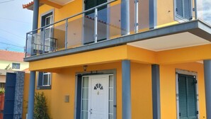 Um edifício de dois andares com varanda, uma porta branca e chão ladrilhado.