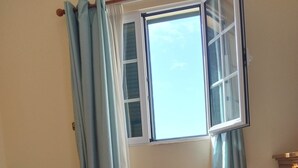 Cama arrumada com uma toalha branca enrolada, janela com cortinas e radiador no chão.
