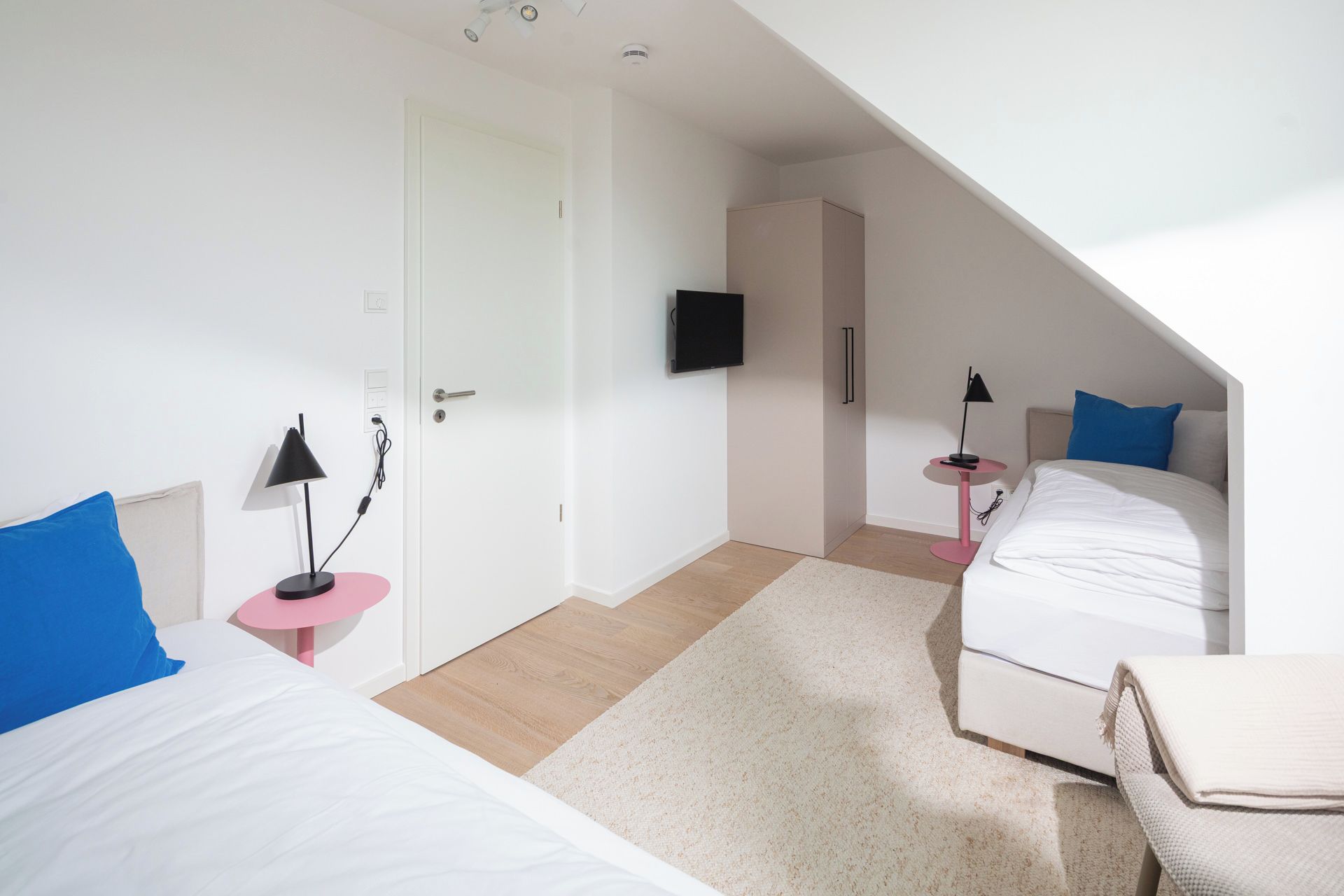 A modern hotel room with two beds, a TV, and a small desk with a lamp.