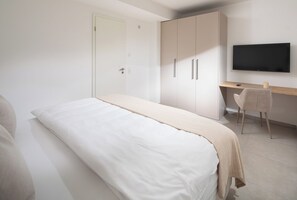 A bedroom with a bed, a desk, a chair, and a television. - // DUNE NEIGHBORHOOD NO. 1 // (Norderney)