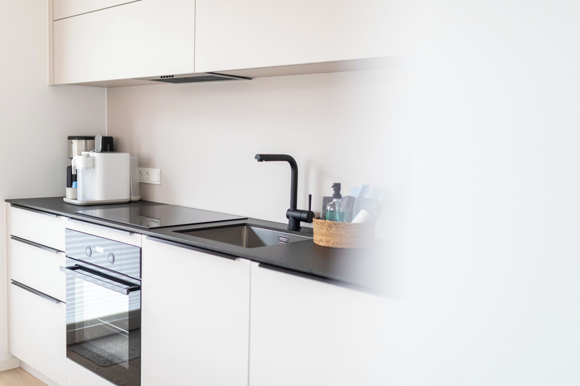 A modern kitchen with a built-in oven, a coffee machine, and a sink with a faucet.