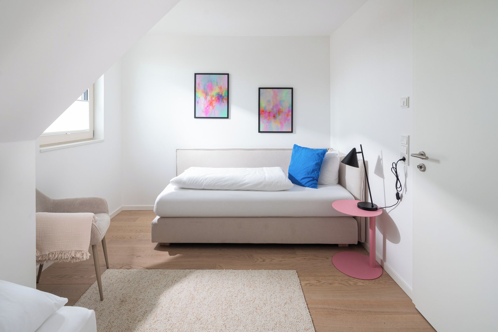 A modern bedroom with a bed, a bedside table, a lamp, and two abstract paintings on the wall.