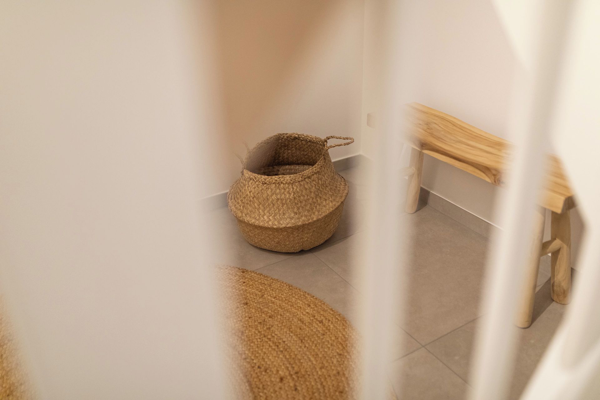 Un panier tressé dans un couloir, avec un banc en bois et un sol carrelé.