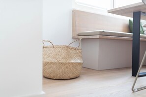 A woven basket on a wooden floor next to a white wall and a window. - // DUNE NEIGHBORHOOD NO. 2 // (Norderney)