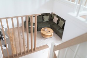 A corner of a room with a sectional sofa, a small round table, and a wooden railing. - // DUNE NEIGHBORHOOD NO. 2 // (Norderney)