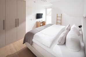 A bedroom with a bed, a desk, a TV, and a wardrobe. - // DUNE NEIGHBORHOOD NO. 2 // (Norderney)