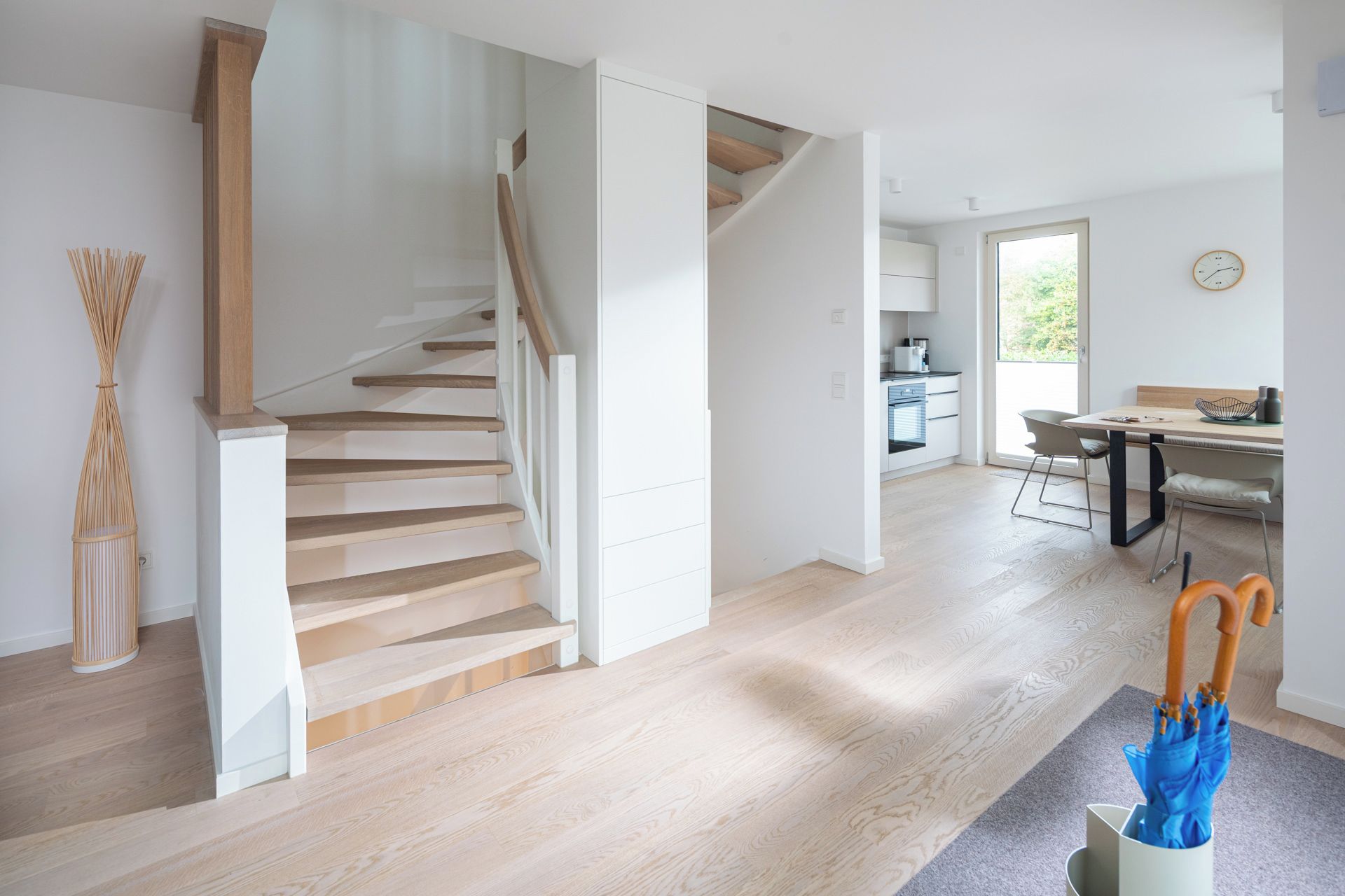 A modern interior with a wooden staircase, a kitchen area, and a dining space.