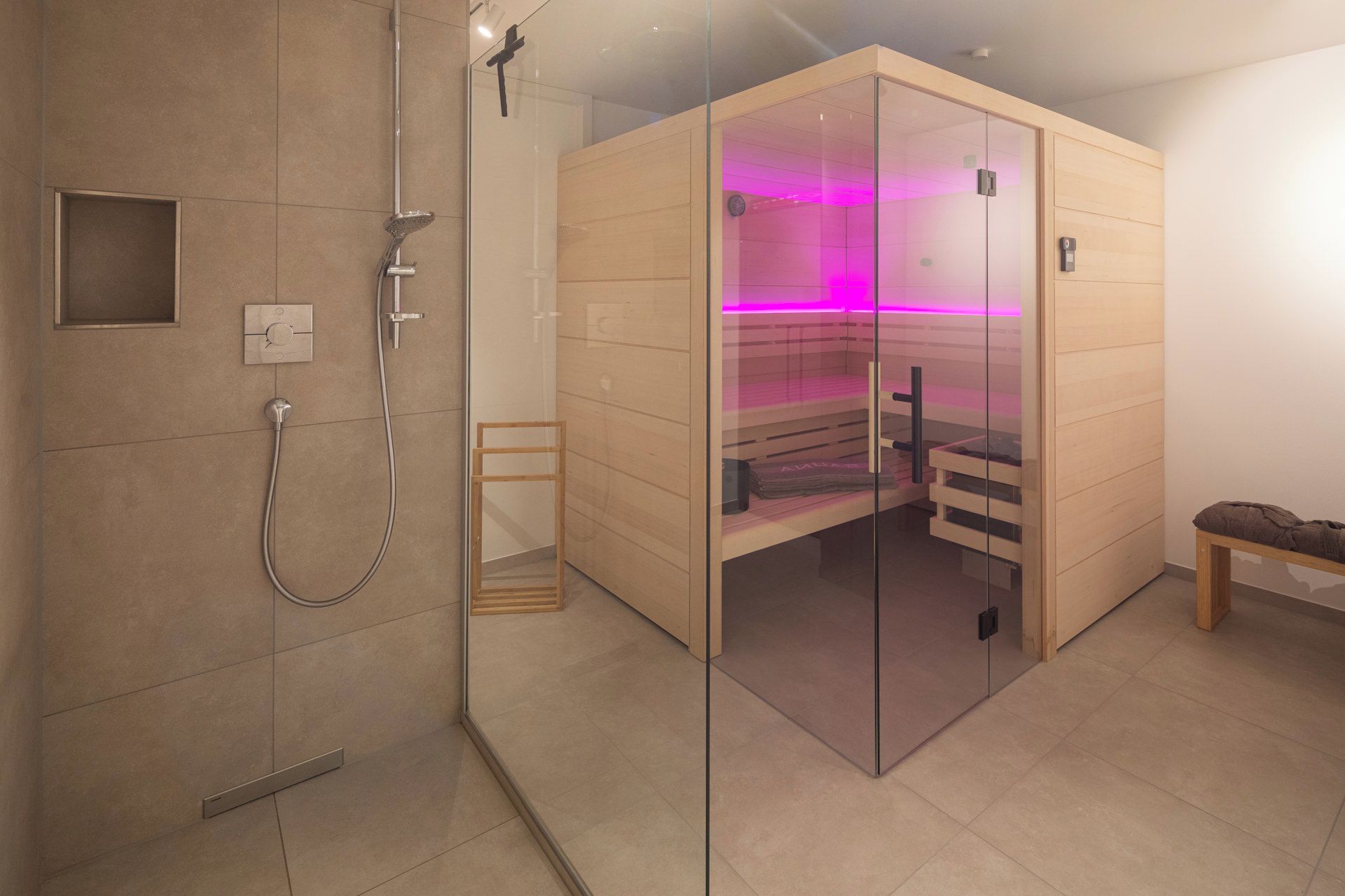 A modern bathroom with a glass-enclosed sauna, a shower area, and a bench.