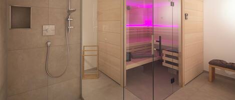 A modern bathroom with a glass-enclosed sauna, a shower area, and a bench.