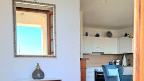 Quarto com piso de madeira, uma mesa com abajur, uma cadeira, cozinha com armários e um espelho na parede.
